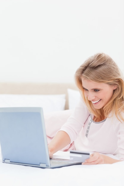 Chiuda in su, donna che per mezzo del computer portatile sul letto mentre esamina lo schermo e sorridere