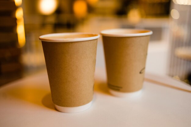 Chiuda in su due tazze di caffè di cartone da asporto sul tavolo sopra la caffetteria del fondo del bokeh e concetto di bevanda da asporto