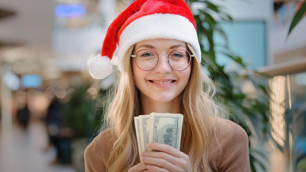 Chiuda in su la signora della donna caucasica ricca che indossa il berretto rosso del cappello di natale della Santa e la rappresentazione felice del monocolo