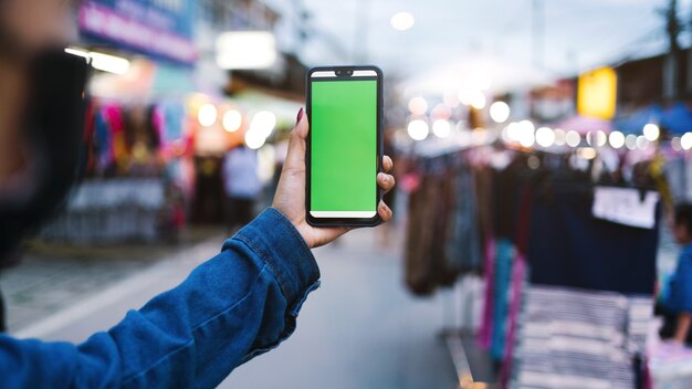 Chiuda in su mobile con schermo verde delle mani che tengono al mercato di strada di notte per camminare in thailandia.