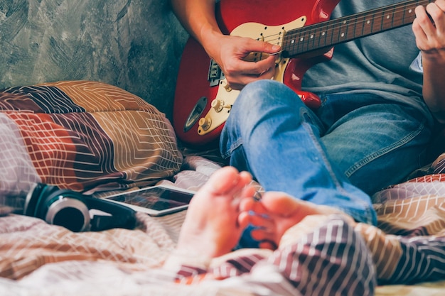 Chiuda su del giovane che gioca la chitarra elettrica sul suo letto, filtro dal grano dei film.