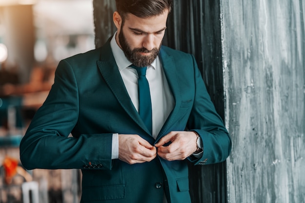 Chiuda su dell'uomo d'affari caucasico bello che abbottona il rivestimento mentre sta all'aperto.