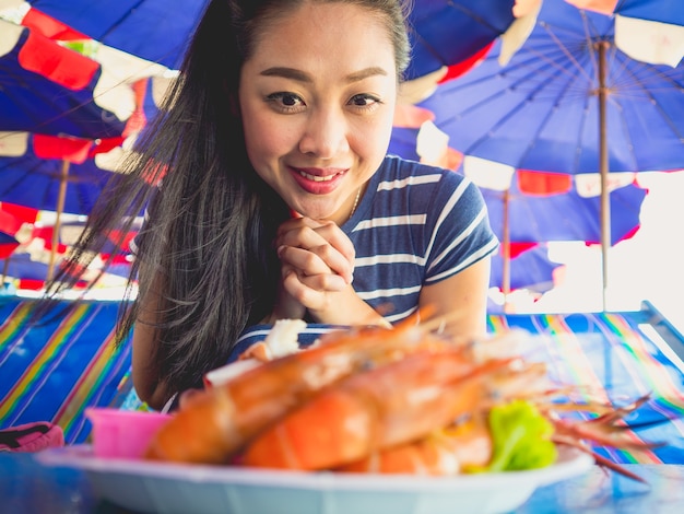 Chiuda su della donna asiatica che mangia i frutti di mare cotti locali della spiaggia della Tailandia.