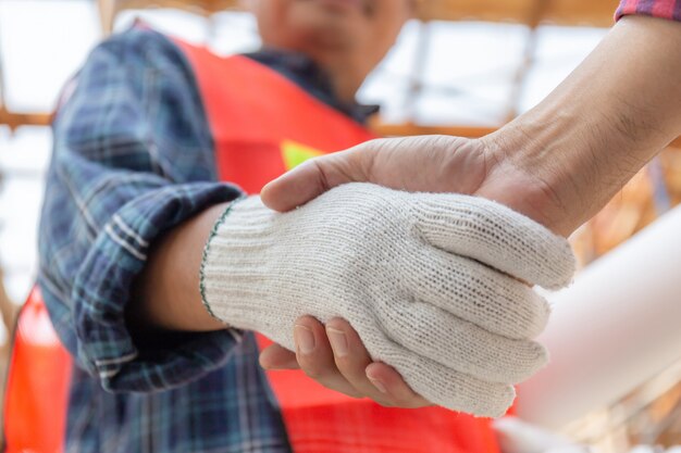 Chiuda su della stretta di mano del lavoratore e dell'ingegnere con il concetto vago del cantiere, di successo e di lavoro di squadra