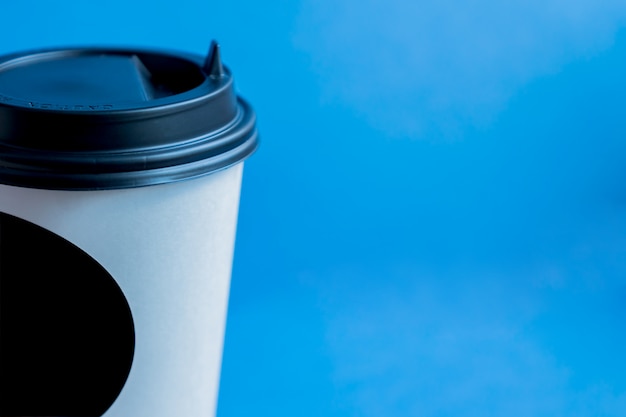 Chiuda su della tazza eliminabile di Kraft del Libro Bianco per caffè con il coperchio di plastica nero sul blu con lo spazio della copia