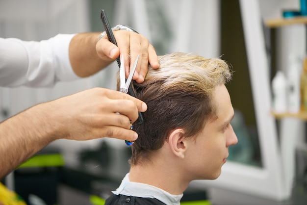 Chiuda su delle mani del barbiere che fanno il nuovo taglio di capelli per il giovane cliente.