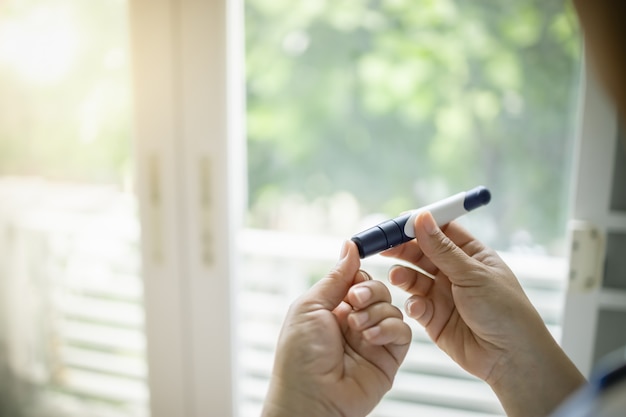 Chiuda su delle mani della donna facendo uso della lancetta sul dito per controllare il livello dello zucchero nel sangue del diabete.