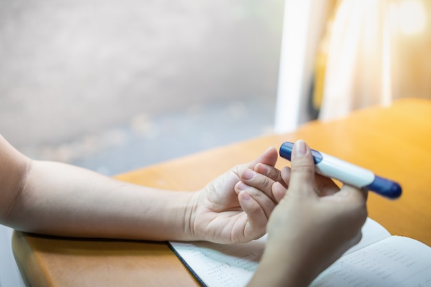 Chiuda su delle mani della donna facendo uso della lancetta sul dito per controllare il livello dello zucchero nel sangue del diabete.