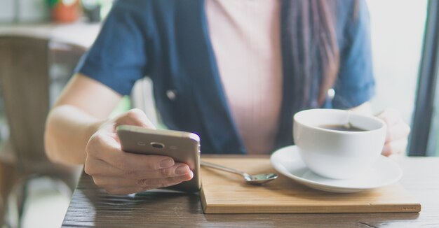 Chiuda su delle mani della giovane donna che tengono lo Smart Phone mobile che si siede in caffè