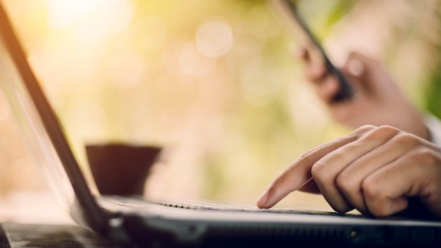 Chiuda su delle mani maschii che scrivono sulla natura del fondo della tastiera del computer portatile