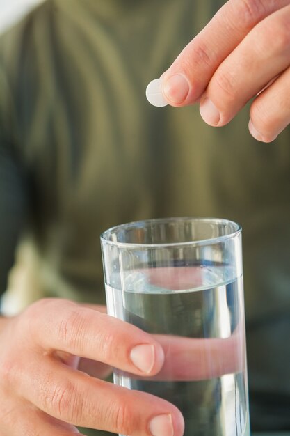 Chiuda su di un uomo che tiene il bicchiere d&#39;acqua e la pillola