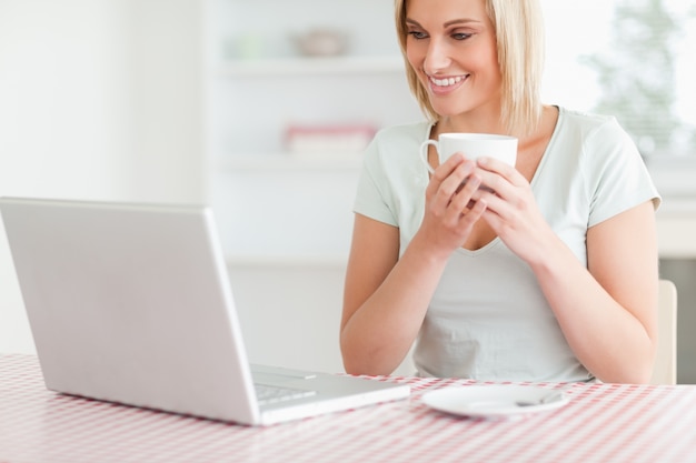 Chiuda su di una donna che tiene il caffè con il computer portatile lei