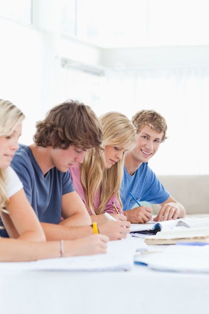 Chiuda su di uno studente che sorride mentre esamina la macchina fotografica mentre studiava con gli amici