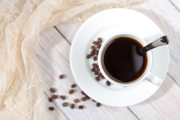 Chiuda su una tazza di caffè caldo con i chicchi di caffè arrostiti sulla tavola di legno bianca.