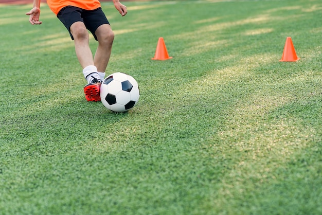 Chiuda sui piedi del calciatore che dà dei calci alla sfera sull'erba.