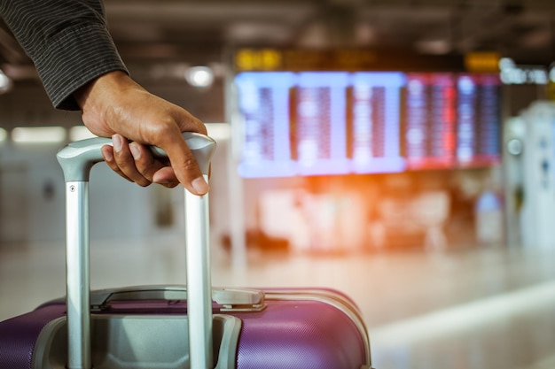 Chiuda sul bagaglio commovente della mano dell'uomo per il check-in all'orario di volo nell'aeroporto internazionale