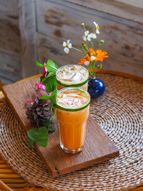 Chiuda sul bicchiere di tè al latte tailandese e caffè freddo con decorazioni floreali sul tavolo vintage in legno al caffè.