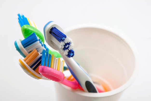 Chiuda sul colpo dell'insieme degli spazzolini da denti multicolori in vetro sulla toilette pulita su fondo bianco, dentale.