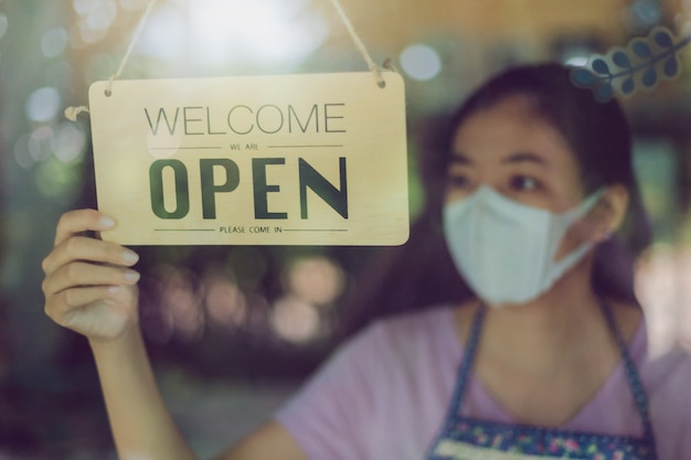 Chiuda sul colpo della scheda d'uso della donna e della mano che girano il bordo aperto del segno sulla porta di vetro in caffetteria.