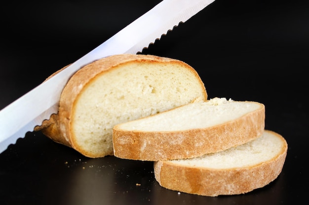 Chiuda sul coltello del pane che affetta attraverso una pagnotta