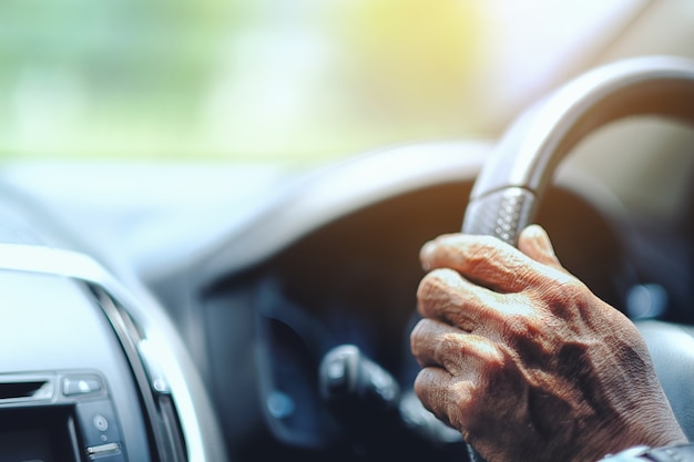 Chiuda sul driver dell&#39;uomo anziano che tiene le mani sul volante