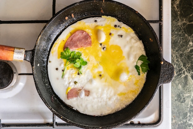 Chiuda sul processo di cottura delle uova scrambled in una padella lubrificata calda con pepe e herbss