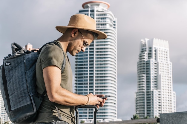 Chiuda sul profilo dell'uomo viaggiatore con un cappello marrone in cerca di direzione sul suo smartphone