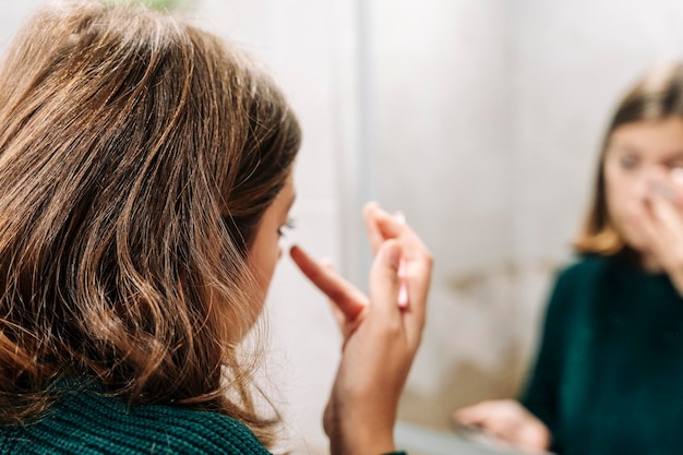 Chiuda sul riflesso dell'adolescente che applica il mascara sulle ciglia