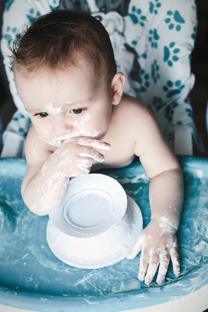 Chiuda sul ritratto del bambino disordinato sveglio che mangia il dessert dolce per la prima volta.