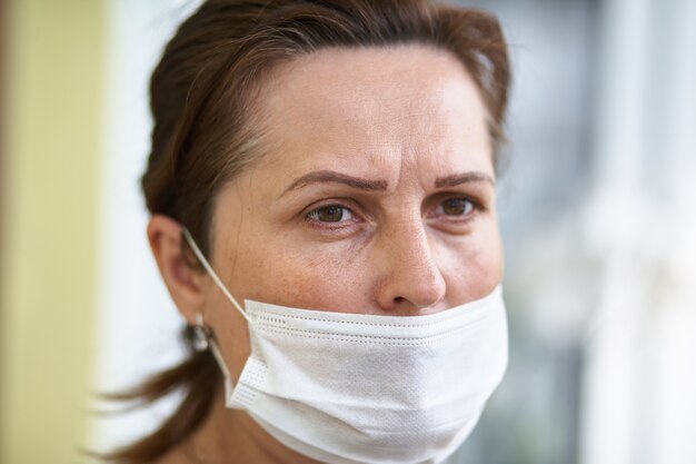 Chiuda sul ritratto della donna che indossa la maschera chirurgica a causa dei virus e dell'inquinamento atmosferico.