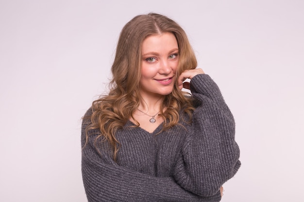 Chiuda sul ritratto della donna tenera caucasica con capelli ricci che indossa cardigan grigio su bianco