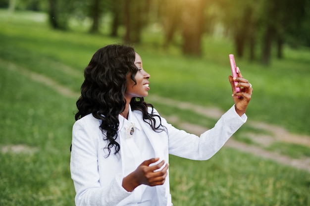 Chiuda sul ritratto della ragazza alla moda dell'afroamericano nero che prende il selfie con il telefono cellulare rosa