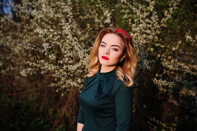 Chiuda sul ritratto della ragazza bionda elegante di Yong al vestito verde sul giardino in primavera degli alberi del fiore.