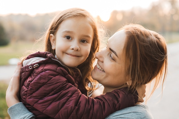 Chiuda sul ritratto di bella giovane madre che abbraccia la sua bambina che sorride all'aperto nel parco.