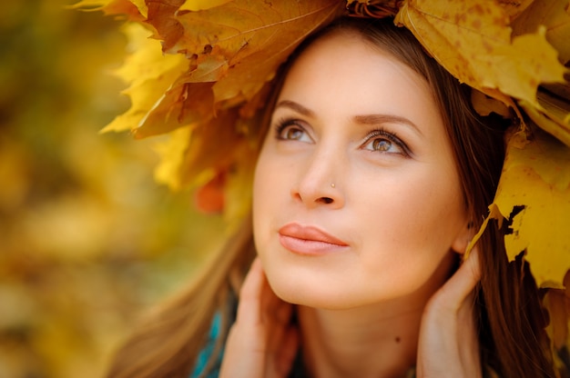 Chiuda sul ritratto di bella ragazza in una maglia scura. Sulla testa è una ghirlanda lussureggiante con foglie d'autunno. La ragazza distoglie lo sguardo.