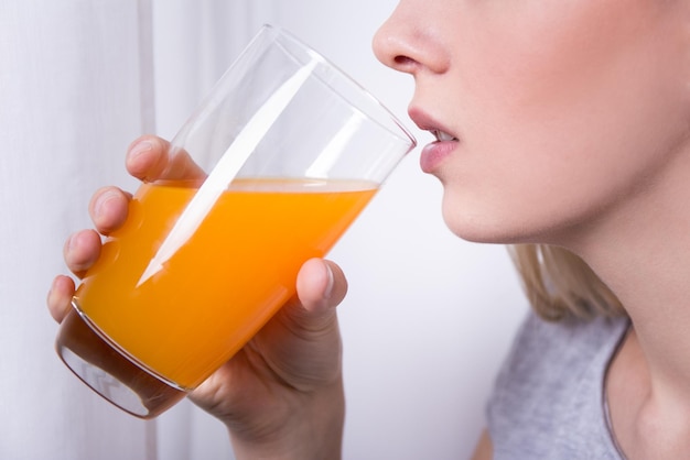 Chiuda sul ritratto di giovane bella donna che beve succo d'arancia