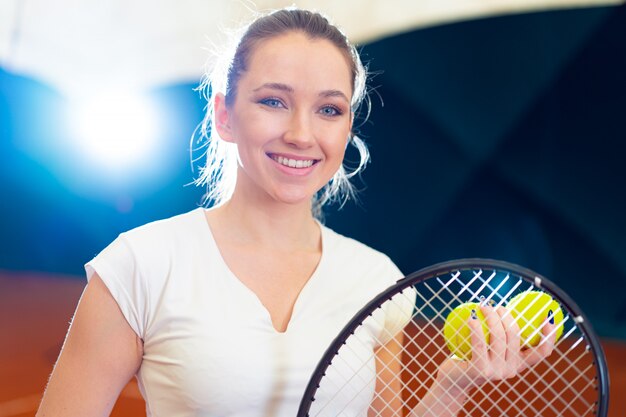 Chiuda sul ritratto di una giovane racchetta di tennis attraente della tenuta del tennis della donna