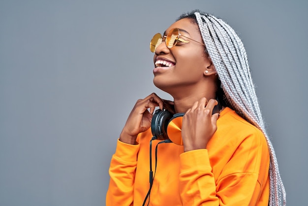 Chiuda sul ritratto di vista laterale della donna afroamericana con gli occhiali da sole che ascolta la musica sugli auricolari
