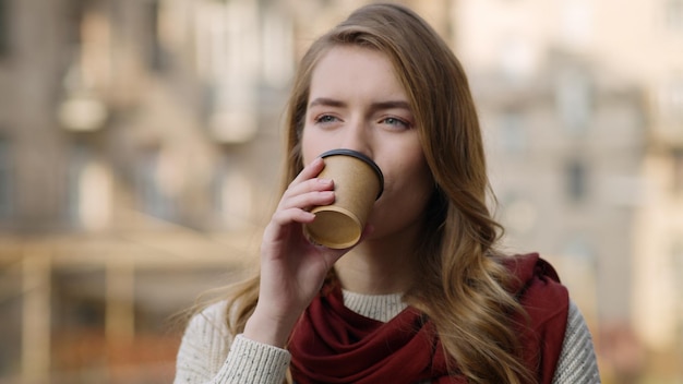 Chiuda sul viso sorridente della donna che beve il tè sulla strada della città Ritratto di bella ragazza hipster godendo del caffè in background urbano Bellezza naturale persona di sesso femminile in piedi con bevanda calda da asporto all'aperto