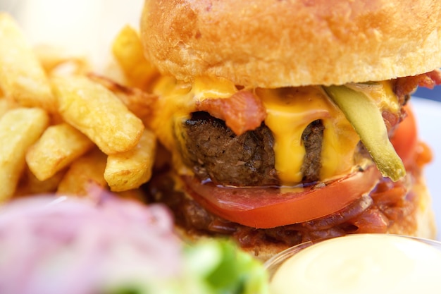 Chiuda sull&#39;hamburger del formaggio e della pancetta con le fritture