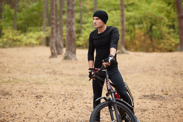 Chiuda sull'immagine del giovane che sta vicino alla sua bici sul sentiero forestale, si ferma per riposare, andare in bicicletta nei fine settimana, passare il tempo libero