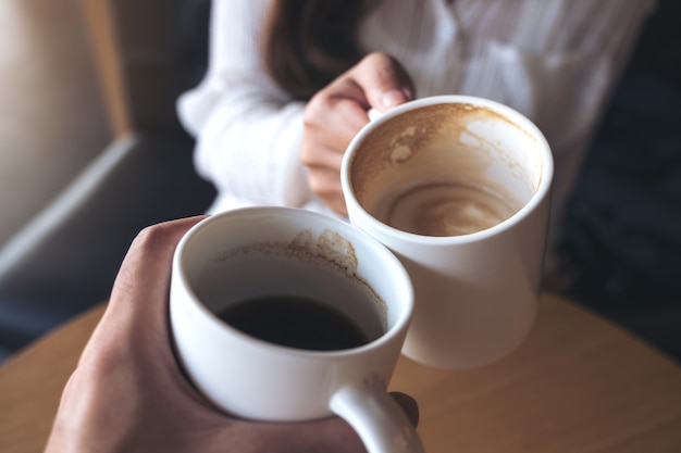 Chiuda sull&#39;immagine di un uomo e una donna tintinnano tazze di caffè bianco nella caffetteria