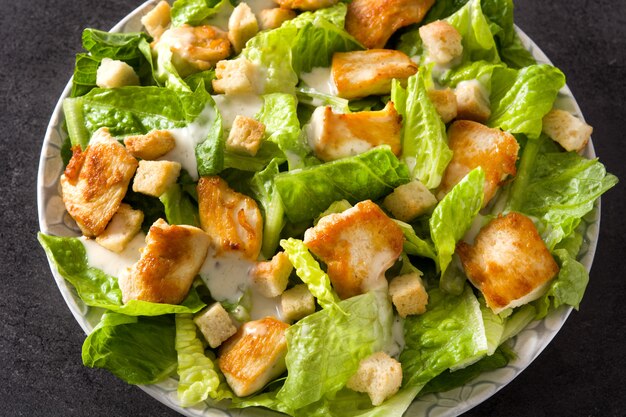 Chiuda sull'insalata di Caesar con lattuga, il pollo e i crostini sul nero