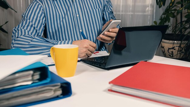 Chiuda sull'uomo che lavora da casa su un computer portatile. Uomo seduto alla scrivania che lavora con il laptop da casa