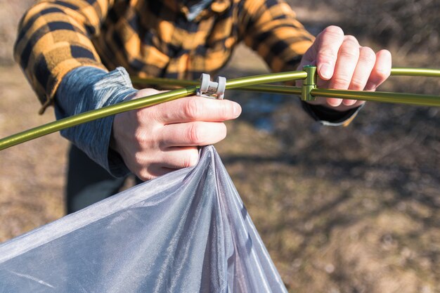 Chiuda sull'uomo di vista in camicia gialla ha installato la tenda in montagne nella primavera