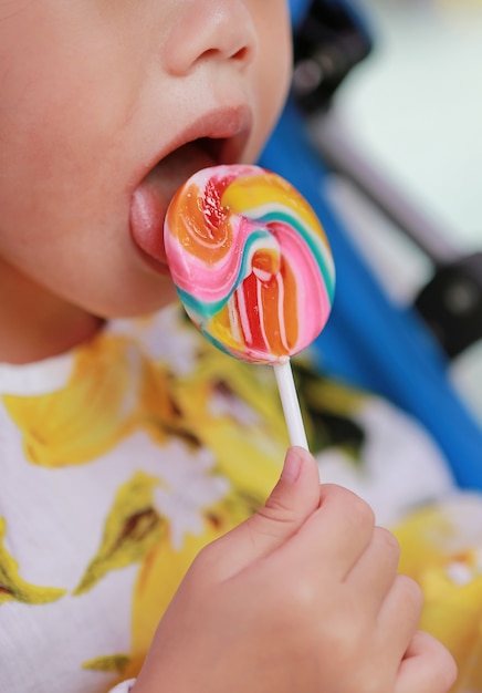 Chiuda sulla bambina che lecca la caramella della lecca-lecca