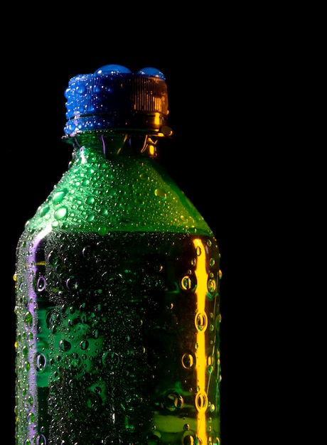 Chiuda sulla bottiglia di plastica verde fredda con le gocce di acqua e sul gelo isolati su fondo nero