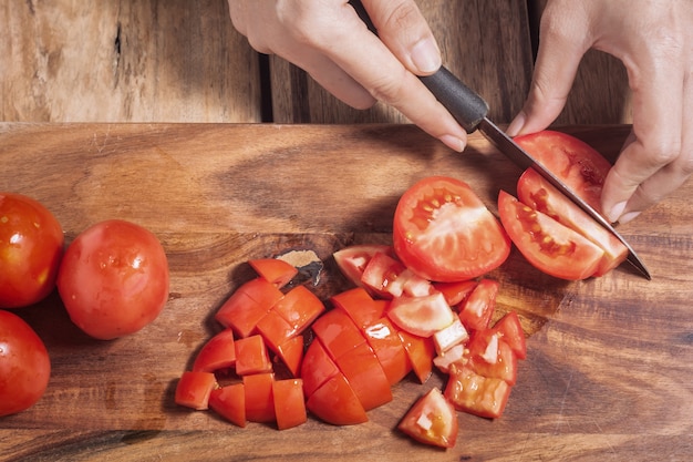 Chiuda sulla casalinga mentre tagliano i pomodori.