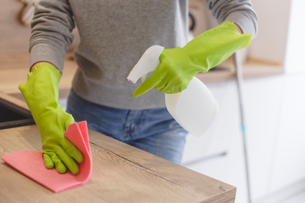 Chiuda sulla cucina di pulizia della donna usando lo spruzzo e il panno della pulitrice.