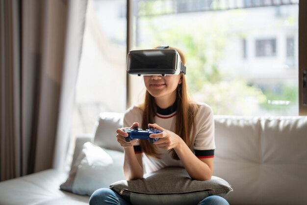 Chiuda sulla donna asiatica di emozione felice che gioca ai videogiochi con il controller su sfondo astratto tonificato con occhiali virtuali